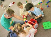 children and childcare worker packing away toys