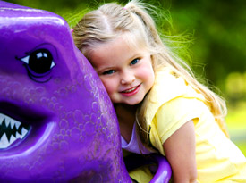 a child sitting on play equipment shaped like a dinosaur.