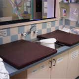 a change bench. There are two change mats on either side of a sink containing a nappy bucket.