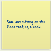 Piece of paper with writing on it saying, 'Sam was sitting on the floor reading a book'.