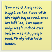 Piece of paper with writing on it saying, 'Sam was sitting cross legged on the floor with his right leg crossed over his left leg. His upper body was hunched over, and he was gripping a book firmly with both hands'.