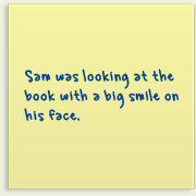 Piece of paper with writing on it saying, 'Sam was staring intently at the book, his eyes bright. His mouth had a wide smile'.