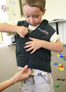 child trying to zip up their jacket. Carer is saying ‘Good work. You were nearly there.’