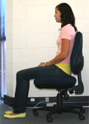 Side view of a person sitting in a chair with their back straight and feet on the floor.