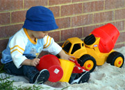 a sandpit with cars, wooden blocks and a watering can sitting neatly on the sand.